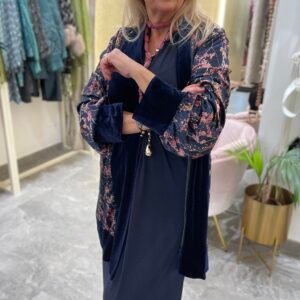 Mujer con vestido azul marino y un kimono de terciopelo azul con estampado floral en tonos rosados. Lleva el mismo collar rosado de la imagen anterior.
