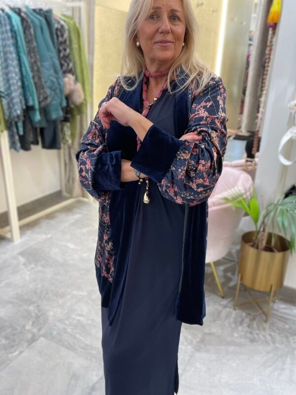 Mujer con vestido azul marino y un kimono de terciopelo azul con estampado floral en tonos rosados. Lleva el mismo collar rosado de la imagen anterior.