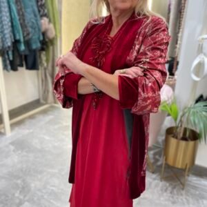 Mujer con vestido rojo y kimono de terciopelo en tonos rojo y negro con estampado floral. Lleva el mismo collar de cuentas rosadas.