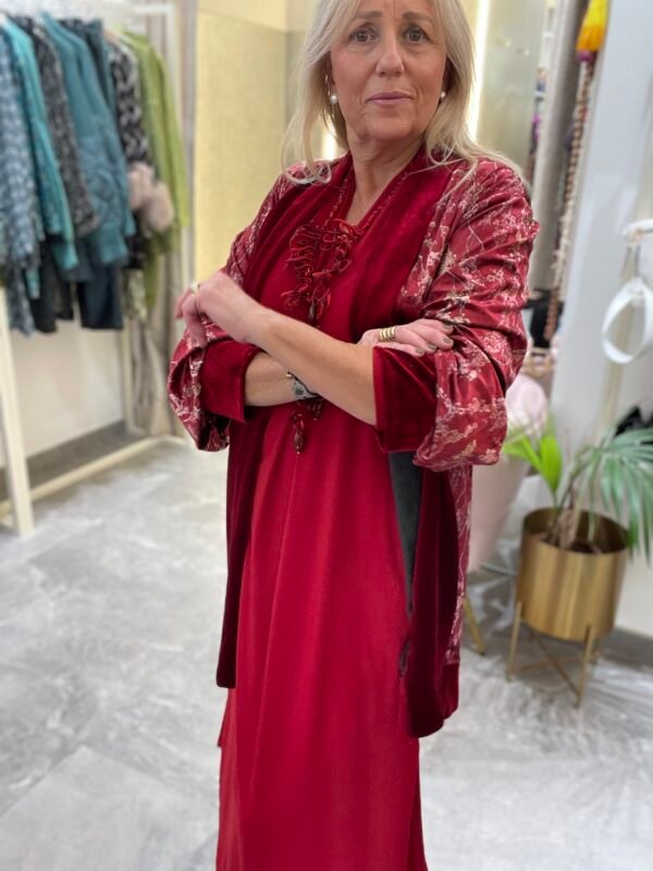Mujer con vestido rojo y kimono de terciopelo en tonos rojo y negro con estampado floral. Lleva el mismo collar de cuentas rosadas.