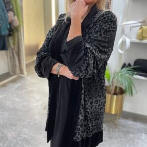 Mujer con vestido negro y kimono gris oscuro con estampado de leopardo. Lleva pendientes de perlas y una expresión seria.