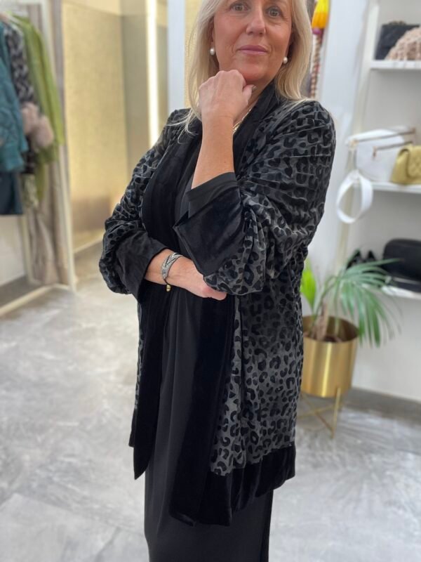 Mujer con vestido negro y kimono gris oscuro con estampado de leopardo. Lleva pendientes de perlas y una expresión seria.