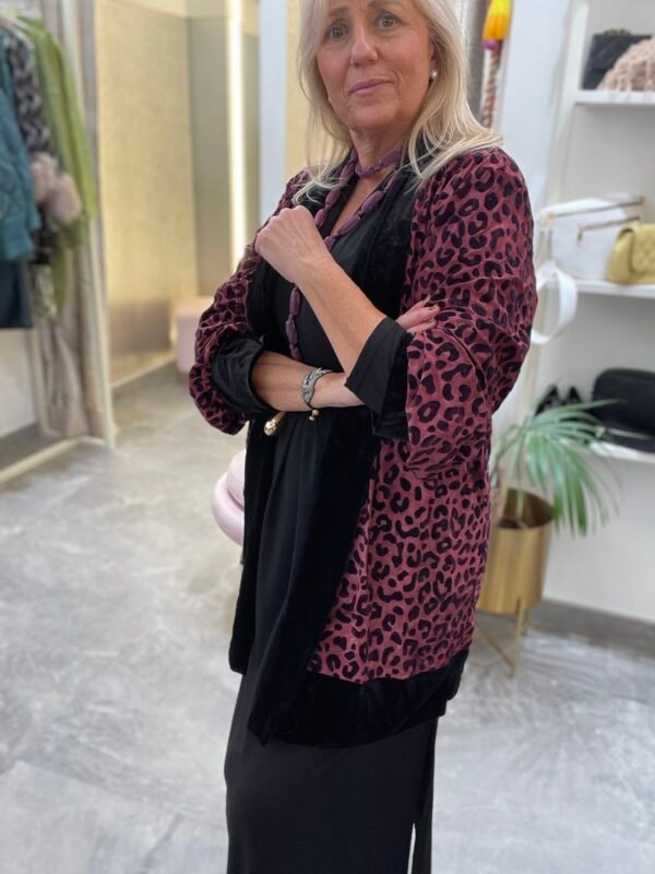 Mujer con vestido negro y kimono de terciopelo en color rosa con estampado de leopardo. Lleva un collar de cuentas rosadas.