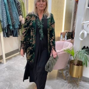 Mujer con vestido negro y kimono verde con estampado de hojas en tonos verdes y marrones. Lleva un collar verde y sostiene una cartera de mano verde.