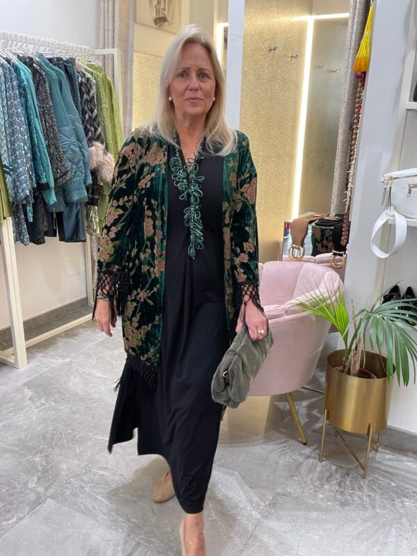 Mujer con vestido negro y kimono verde con estampado de hojas en tonos verdes y marrones. Lleva un collar verde y sostiene una cartera de mano verde.