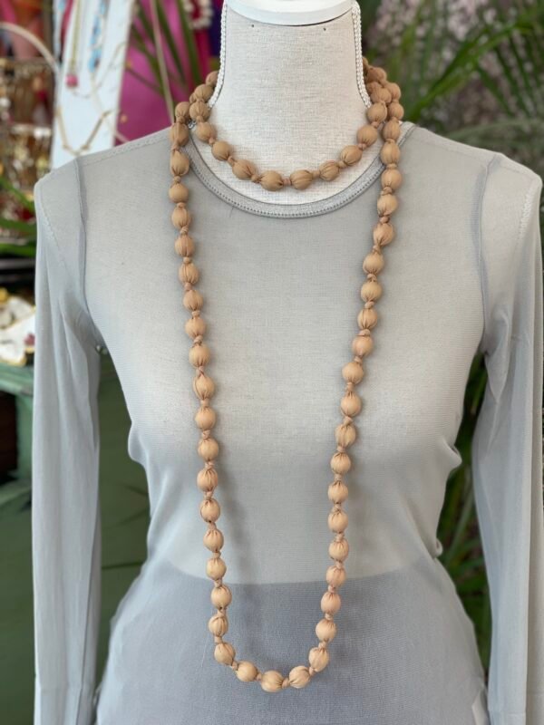 Collar doble de cuentas grandes envueltas en tela beige, mostrado en un busto de tela gris claro.