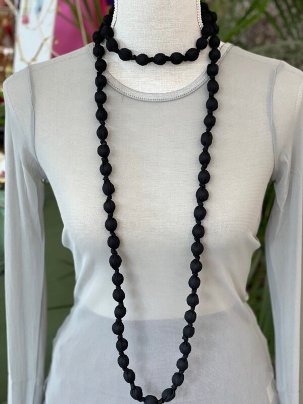 Collar doble de cuentas grandes envueltas en tela negra, exhibido en un busto de tela gris claro.
