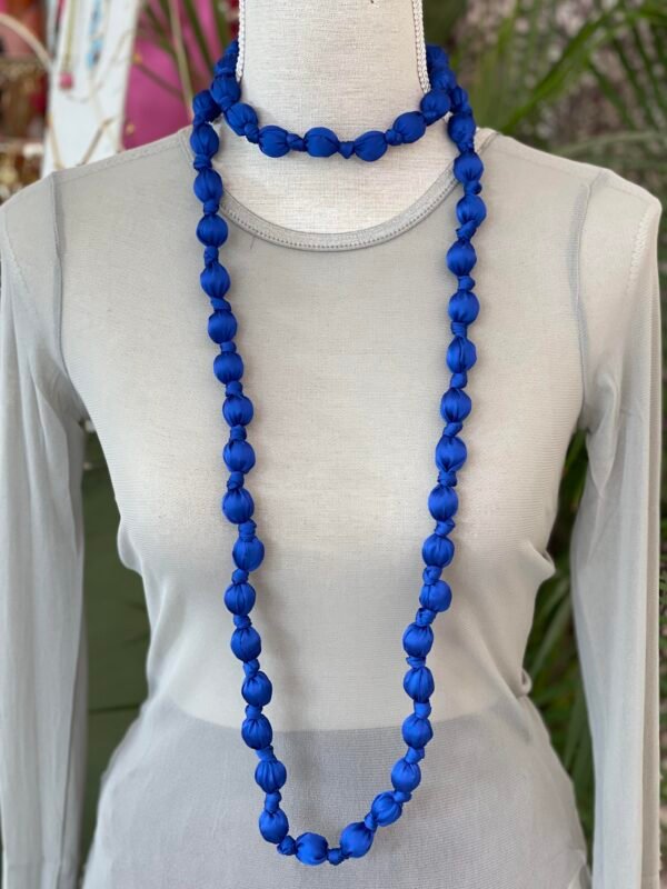 Collar doble de cuentas grandes envueltas en tela azul intenso, mostrado en un busto de tela gris claro.