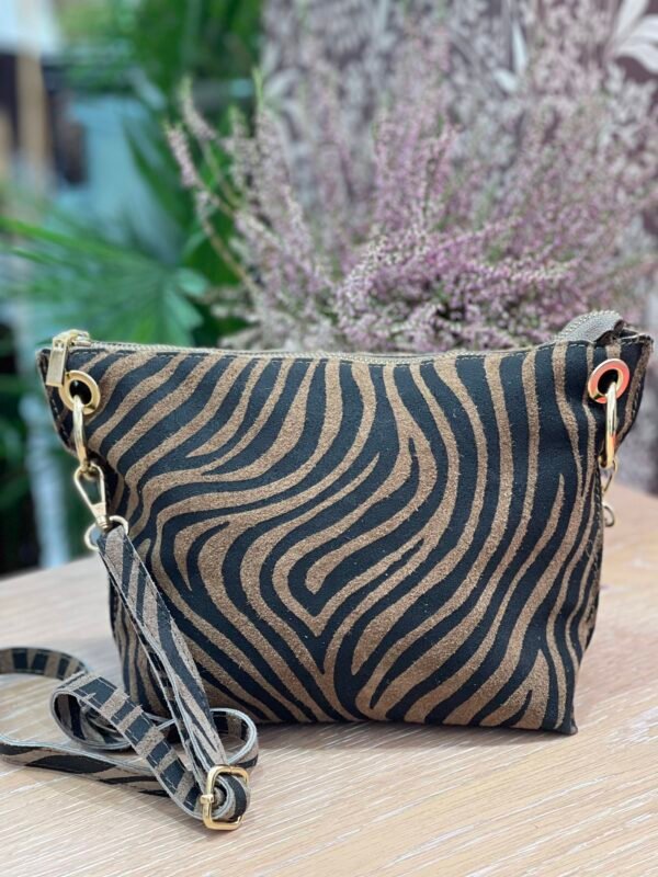 Bolso pequeño con estampado de cebra en tonos marrón y negro, con asa desmontable a juego, sobre una superficie de madera clara.