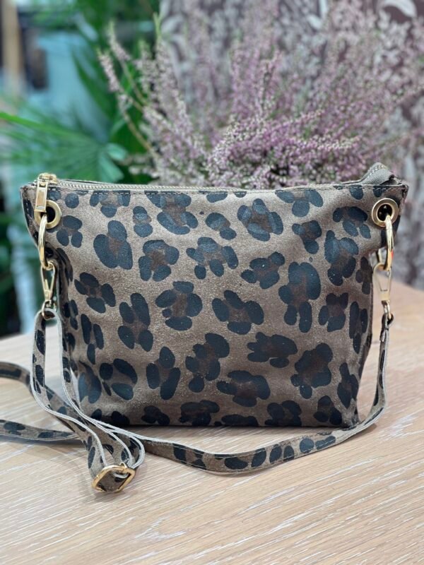 Bolso pequeño con estampado de manchas en tonos marrón oscuro sobre un fondo beige, con asa desmontable a juego, sobre una superficie de madera clara.