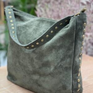 Bolso grande de gamuza verde oliva con detalles de tachuelas doradas en el asa y los laterales, sobre una superficie de madera clara.