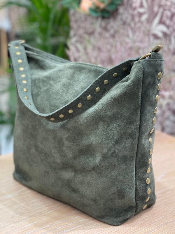 Bolso grande de gamuza verde oliva con detalles de tachuelas doradas en el asa y los laterales, sobre una superficie de madera clara.