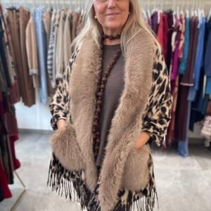 Mujer con un abrigo de estampado de leopardo y cuello de peluche beige. Lleva un collar de cuentas marrones y ropa oscura, con un fondo de ropa en exhibición.