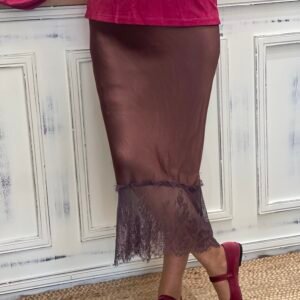 Mujer con falda satinada marrón con encaje en el borde inferior y zapatos Mary Jane en terciopelo fucsia, sobre una alfombra de yute.
