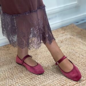 Detalle de falda marrón con encaje en el borde inferior y zapatos Mary Jane fucsia de terciopelo, sobre una alfombra de yute.