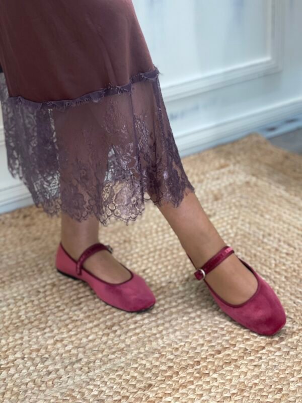 Detalle de falda marrón con encaje en el borde inferior y zapatos Mary Jane fucsia de terciopelo, sobre una alfombra de yute.